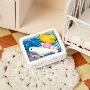 Miniature nursery toy basket displayed beside crib, charming dollhouse baby room decor with playful bath accessories and soft handmade feel