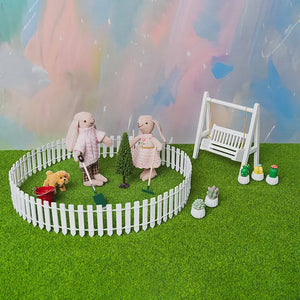 Milo and Clara planting a tree in a dollhouse garden scene with tools and watering bucket.