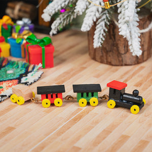 Colorful wooden toy train displayed beside Christmas gifts and a snowy tree, adding nostalgic charm to a holiday dollhouse.