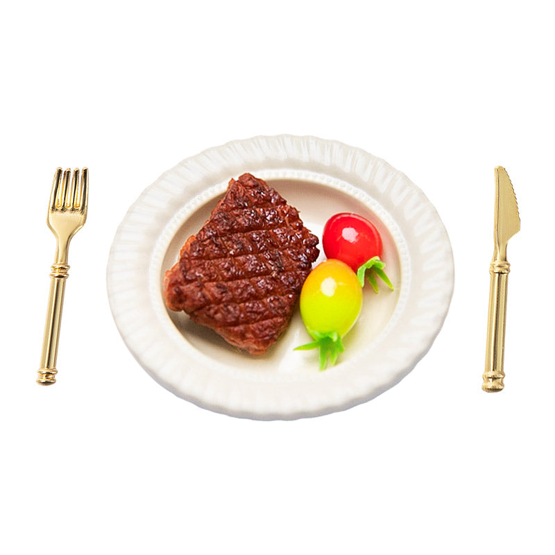 White background image of a handcrafted clay steak with two clay tomatoes, a miniature plate, and cutlery for a 1:12 scale dollhouse