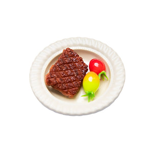 White background image of a handcrafted clay steak with two clay tomatoes, a miniature plate, and cutlery for a 1:12 scale dollhouse