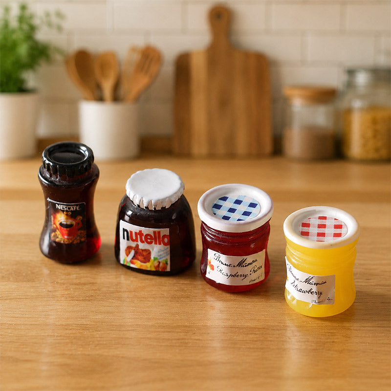 Colorful miniature pantry jars including jams and coffee, styled on a dollhouse countertop for charming everyday kitchen play.