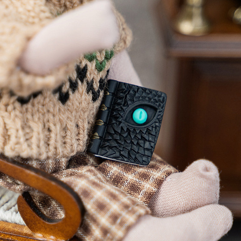Textured black grimoire with a turquoise dragon eye, styled in a cozy witch’s study for a magical Halloween scene