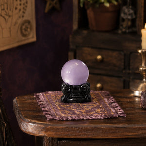 Purple crystal ball resting on a tiny cloth atop a wooden table, adding dreamy charm to a witch’s study or magic room.