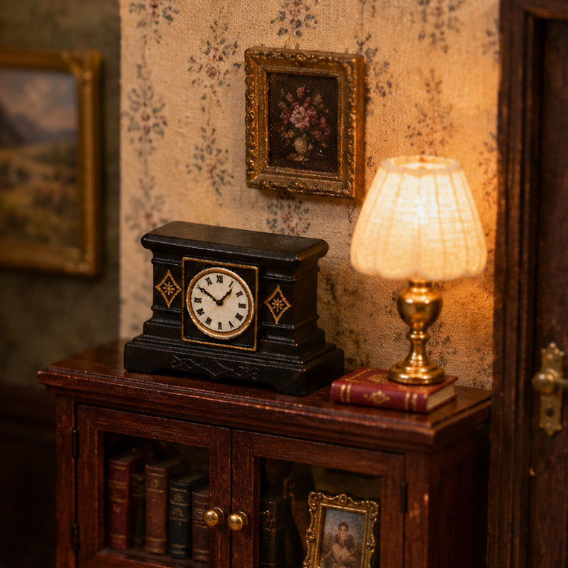 Vintage black mantel clock styled with a glowing lamp, books, and framed art on a cozy dollhouse cabinet.