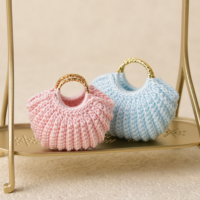 Pink and light blue miniature crochet handbags shown together, highlighting soft yarn texture and delicate gold handles