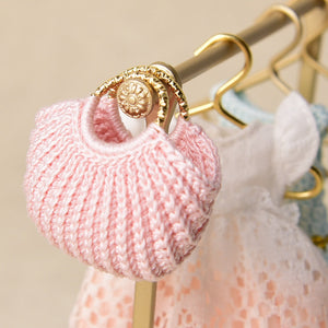Pink miniature yarn handbag hanging beside tiny clothes, creating a sweet and playful dressing-room detail