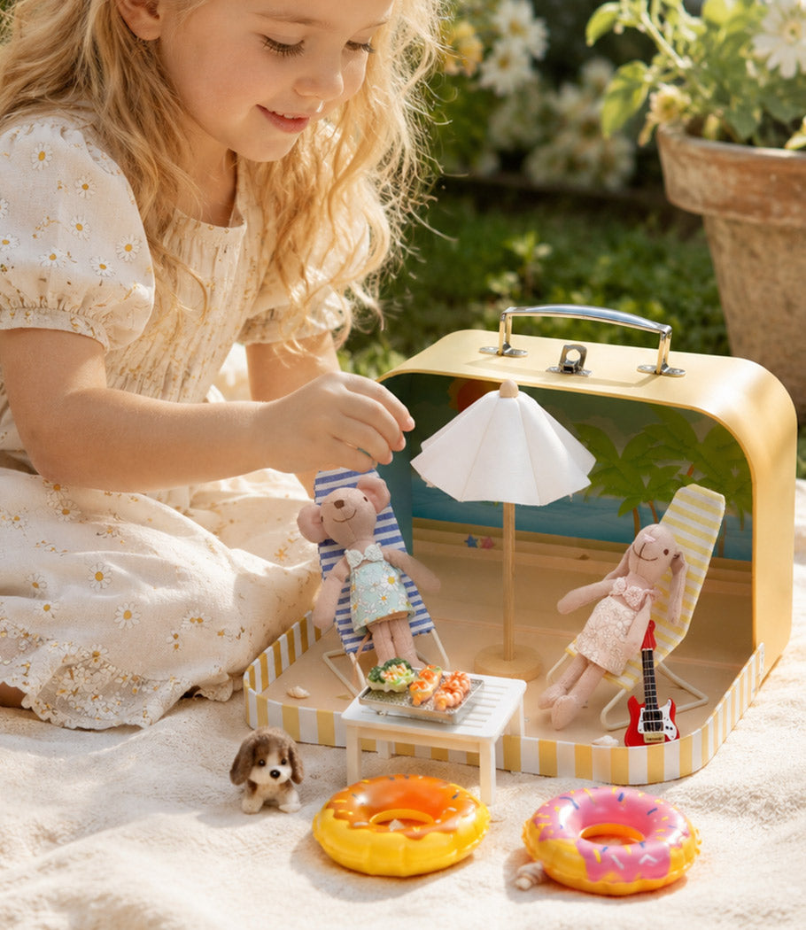 Child playing with dollhouse beach accessories, tiny friends, lounge chairs and umbrella in a sunny outdoor scene