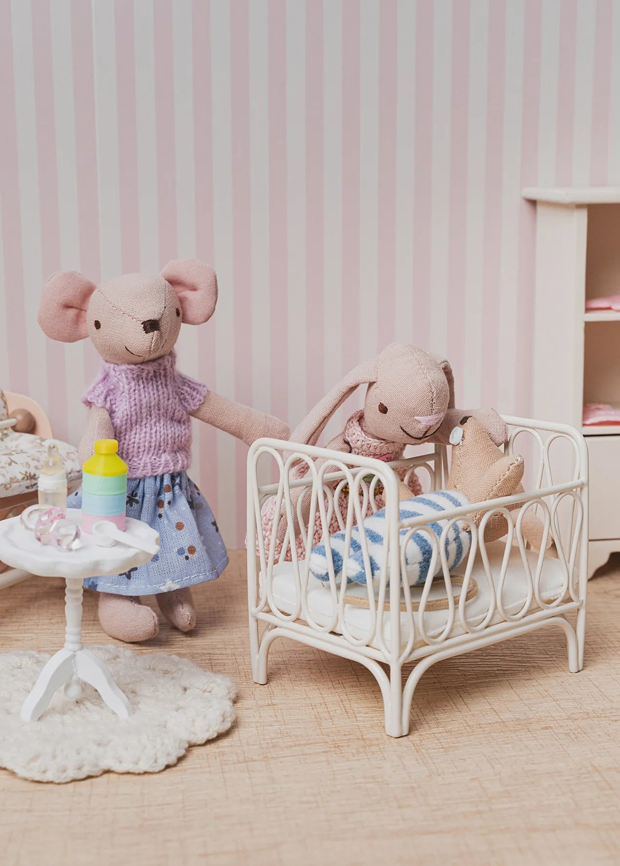 Cozy nursery scene with caring dollhouse friends, featuring a baby crib, feeding table, and soft bedroom decor for heartwarming 1:12 scale storytelling.