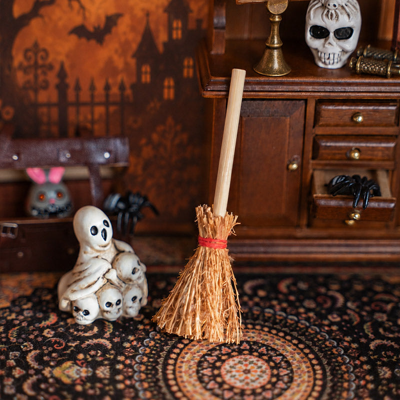 Miniature witch broom and little ghost figures styled on a vintage rug for a playful Halloween study scene
