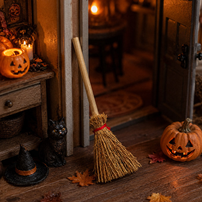 Rustic miniature broom by a dollhouse doorway with pumpkins and a black cat, styled for a warm witchy Halloween scene.