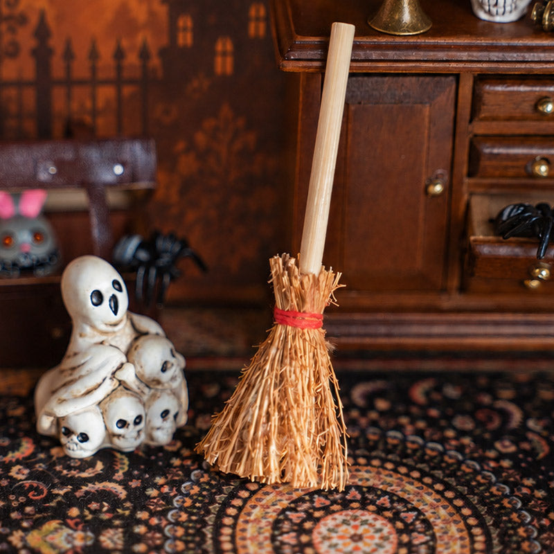 Rustic miniature broom with bundled bristles styled on a vintage rug with spooky figures in a cozy witchy study