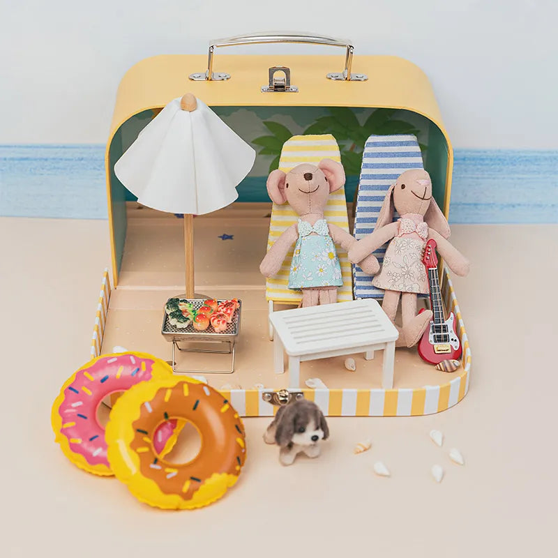 Miniature beach scene inside a portable dollhouse case with tiny furniture, creating a sunny seaside story world