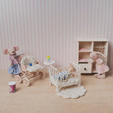dollhouse nursery scene with crib stroller wardrobe and miniature figures in a soft pink 1:12 scale storytelling setup.