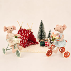 Two little mouse friends ride flower-filled tricycles beside a cozy tent and gifts for a sweet holiday outing