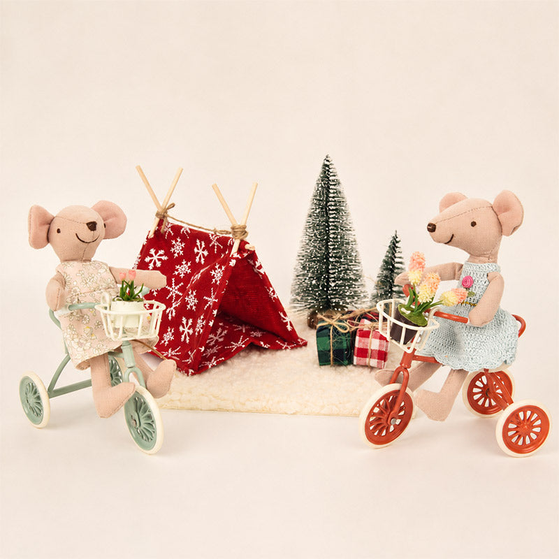 Two little mouse friends ride flower-filled tricycles beside a cozy tent and gifts for a sweet holiday outing