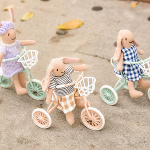 Three bunny friends ride colorful miniature tricycles with baskets along a playful outdoor path together
