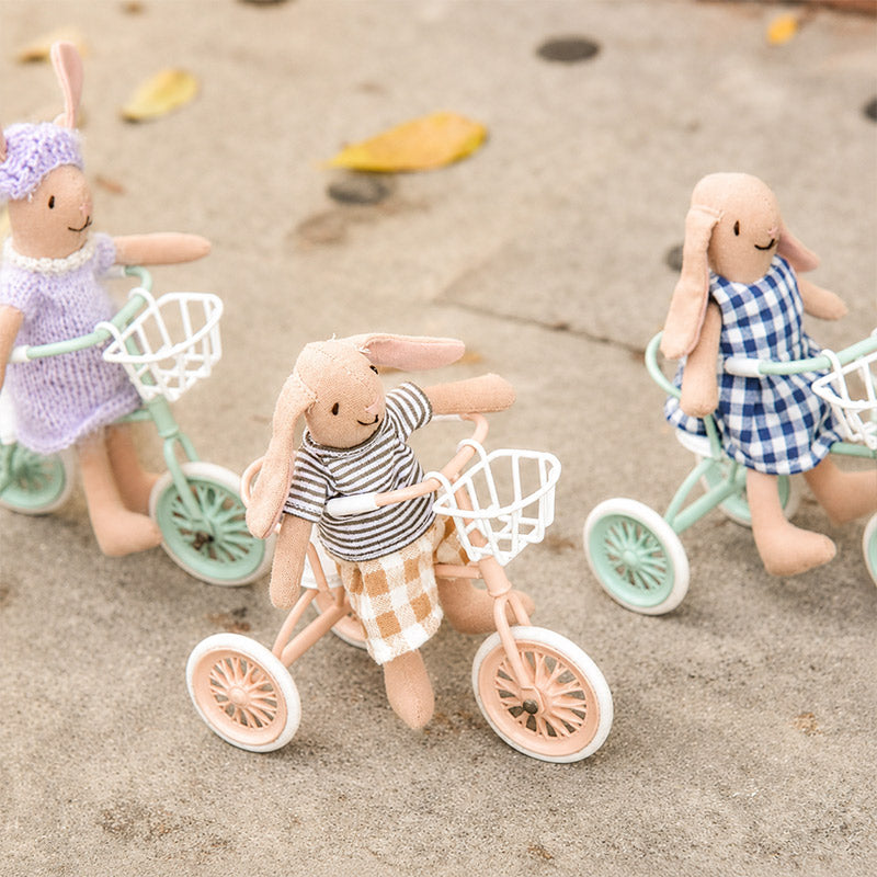 Three bunny friends ride colorful miniature tricycles with baskets along a playful outdoor path together