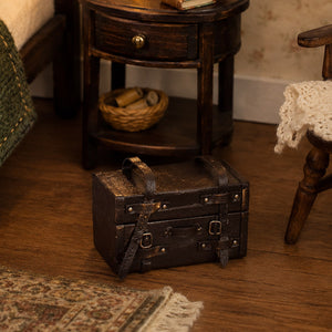 Vintage dollhouse luggage beside a wooden nightstand and chair, adding a warm traveled feel to a cozy bedroom.