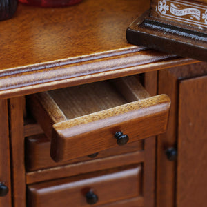 Vintage miniature cabinet with an open drawer and dark knobs, showing warm wood grain and functional storage