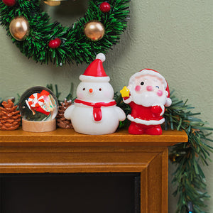 Tiny Santa and snowman decorations displayed beside a snow globe and pinecones on a warmly decorated Christmas mantel.