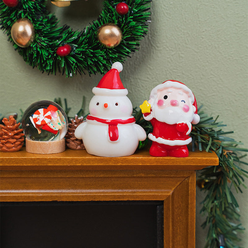 Tiny Santa and snowman decorations displayed beside a snow globe and pinecones on a warmly decorated Christmas mantel.