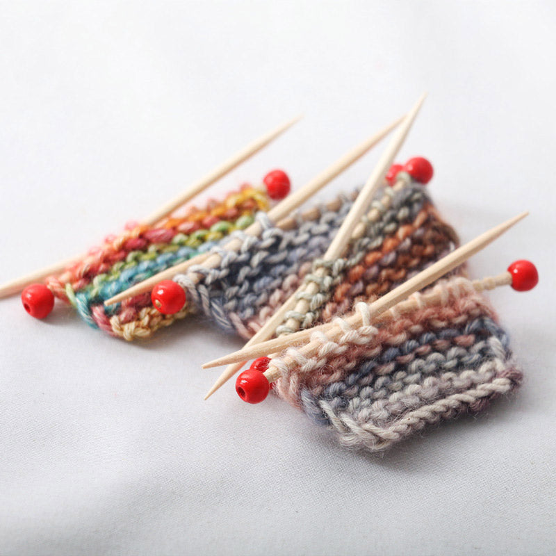 Tiny knitted yarn pieces with wooden needles and soft multicolor textures, perfect for a warm miniature craft corner.