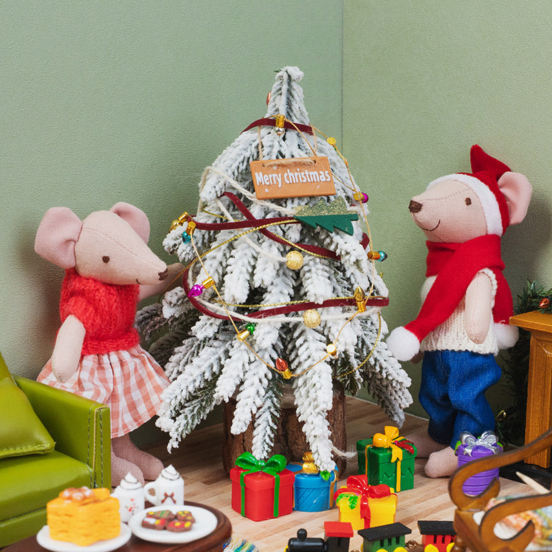 Miniature Merry Christmas hanging sign decorating a snowy Christmas tree as two little mice gather beside colorful gifts.