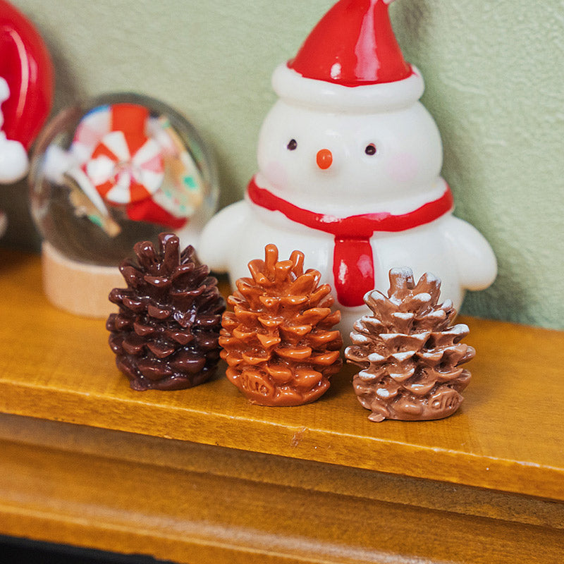Miniature Christmas pinecones arranged beside a cheerful snowman on a wooden mantel for a warm holiday display.
