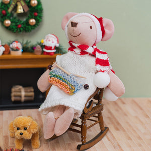 Handmade mother mouse doll knitting in a wooden rocking chair beside a cozy fireplace, creating a peaceful Christmas scene.