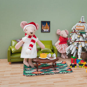 Christmas mouse doll with her family beside a snowy tree, green sofa, and festive treats in a cozy miniature living room.